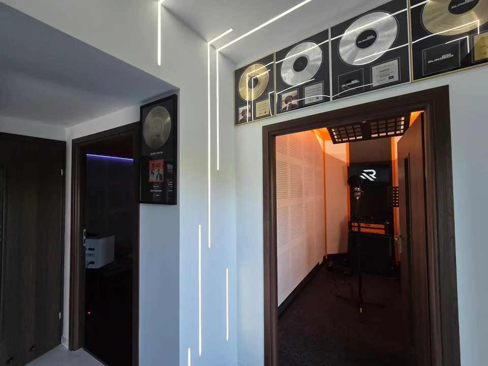 Korytarz Ramzes Studio, ściana z płytami i wejście do oświetlonej kabiny nagraniowej